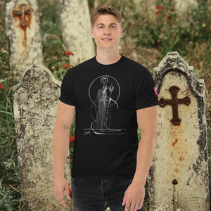 Man wearing a black Saint of Shadows t-shirt with white line art of Death holding a skull, framed by halo-like geometry, standing among aged gravestones.
