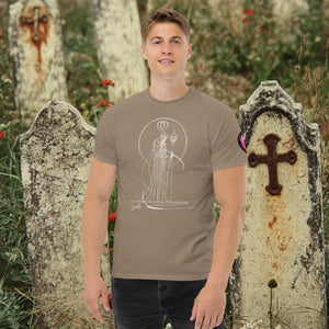 Man wearing a brown Savana Saint of Shadows t-shirt with white line art of Death holding a skull, framed by halo-like geometry, standing among aged gravestones.