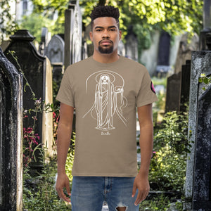 Man wearing a brown savana Arcane Guardian t-shirt with white skeletal line art and all-seeing symbol, standing in a sunlit graveyard.