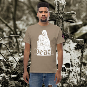 Man wearing a brown savana Death’s Embrace t-shirt featuring skeleton holding a woman, gothic lettering reading “Death,” standing before a weathered grave.