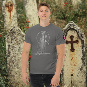 Man wearing a charcoal Saint of Shadows t-shirt with white line art of Death holding a skull, framed by halo-like geometry, standing among aged gravestones.