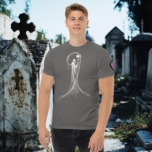 Man wearing a charcoal front Veil of Solitude t-shirt with white line art of the Grim Reaper lifting a skull, standing among sunlit mausoleums in a cemetery.