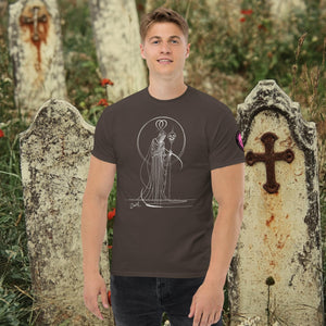Man wearing a dark chocolate Saint of Shadows t-shirt with white line art of Death holding a skull, framed by halo-like geometry, standing among aged gravestones.