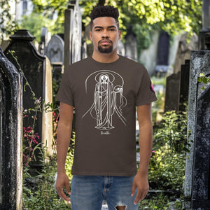 Man wearing a dark chocolate Arcane Guardian t-shirt with white skeletal line art and all-seeing symbol, standing in a sunlit graveyard.