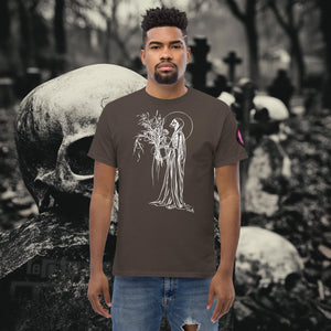Man wearing a dark chocolate Reaper’s Harvest t-shirt with white line art of a skeletal figure holding flowers, standing before a background of skulls and gravestones.