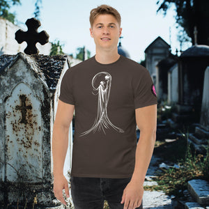 Man wearing a dark chocolate Veil of Solitude t-shirt with white line art of the Grim Reaper lifting a skull, standing among sunlit mausoleums in a cemetery.
