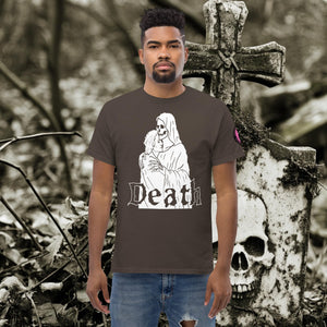 Man wearing a dark chocolate Death’s Embrace t-shirt featuring skeleton holding a woman, gothic lettering reading “Death,” standing before a weathered grave.