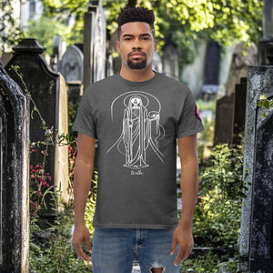 Man wearing a dark heather Arcane Guardian t-shirt with white skeletal line art and all-seeing symbol, standing in a sunlit graveyard.