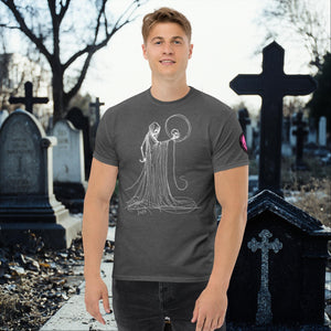 Man wearing a dark heather Eternal Vigil t-shirt with white line art of a robed figure holding a skull, standing in a cemetery surrounded by tombstones.