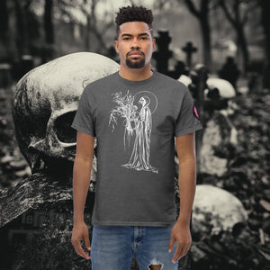 Man wearing a dark heather Reaper’s Harvest t-shirt with white line art of a skeletal figure holding flowers, standing before a background of skulls and gravestones.