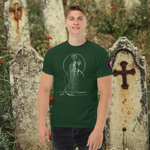 Man wearing a forest green Saint of Shadows t-shirt with white line art of Death holding a skull, framed by halo-like geometry, standing among aged gravestones.
