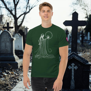 Man wearing a forest green Eternal Vigil t-shirt with white line art of a robed figure holding a skull, standing in a cemetery surrounded by tombstones.