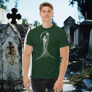 Man wearing a forest green Veil of Solitude t-shirt with white line art of the Grim Reaper lifting a skull, standing among sunlit mausoleums in a cemetery.