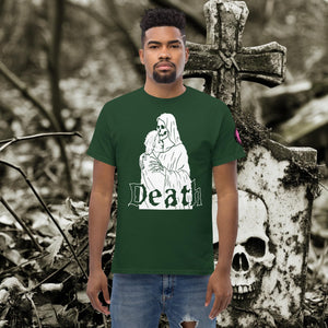 Man wearing a forest green Death’s Embrace t-shirt featuring skeleton holding a woman, gothic lettering reading “Death,” standing before a weathered grave.