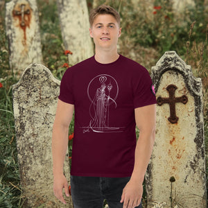 Man wearing a maroon Saint of Shadows t-shirt with white line art of Death holding a skull, framed by halo-like geometry, standing among aged gravestones.