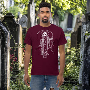 Man wearing a maroon Arcane Guardian t-shirt with white skeletal line art and all-seeing symbol, standing in a sunlit graveyard.