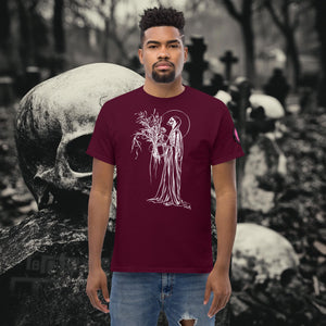 Man wearing a maroon Reaper’s Harvest t-shirt with white line art of a skeletal figure holding flowers, standing before a background of skulls and gravestones.