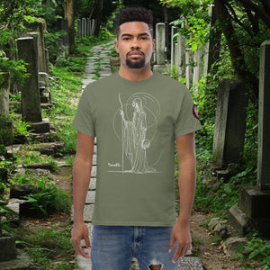Man wearing a military green Grim Sentinel t-shirt with white line art of a cloaked reaper holding a scythe and skull, standing on a mossy cemetery path.