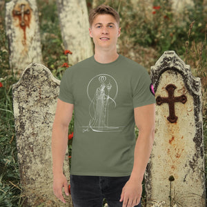 Man wearing a military green Saint of Shadows t-shirt with white line art of Death holding a skull, framed by halo-like geometry, standing among aged gravestones.