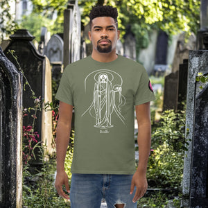 Man wearing a military green Arcane Guardian t-shirt with white skeletal line art and all-seeing symbol, standing in a sunlit graveyard.
