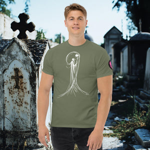 Man wearing a military green Veil of Solitude t-shirt with white line art of the Grim Reaper lifting a skull, standing among sunlit mausoleums in a cemetery.