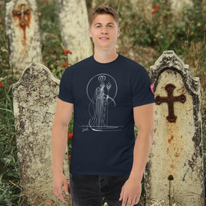 Man wearing a navy Saint of Shadows t-shirt with white line art of Death holding a skull, framed by halo-like geometry, standing among aged gravestones.