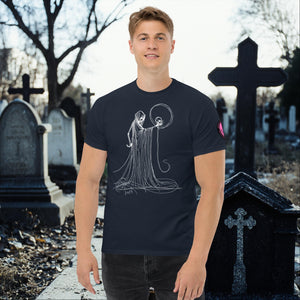 Man wearing a navy Eternal Vigil t-shirt with white line art of a robed figure holding a skull, standing in a cemetery surrounded by tombstones.
