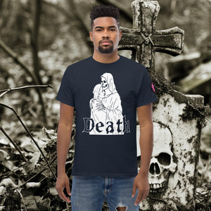 Man wearing a navy Death’s Embrace t-shirt featuring skeleton holding a woman, gothic lettering reading “Death,” standing before a weathered grave.