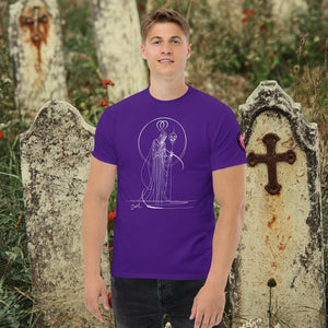 Man wearing a purple Saint of Shadows t-shirt with white line art of Death holding a skull, framed by halo-like geometry, standing among aged gravestones.