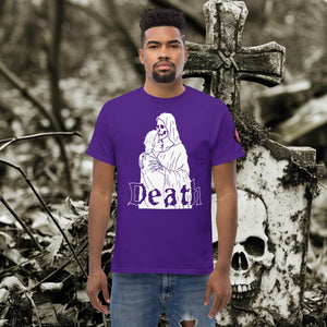 Man wearing a purple Death’s Embrace t-shirt featuring skeleton holding a woman, gothic lettering reading “Death,” standing before a weathered grave.