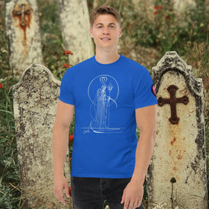 Man wearing a royal blue Saint of Shadows t-shirt with white line art of Death holding a skull, framed by halo-like geometry, standing among aged gravestones.