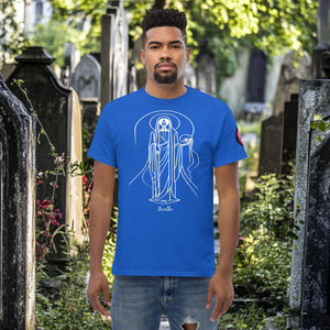 Man wearing a royal blue Arcane Guardian t-shirt with white skeletal line art and all-seeing symbol, standing in a sunlit graveyard.