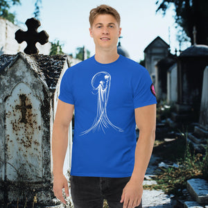 Man wearing a royal blue Veil of Solitude t-shirt with white line art of the Grim Reaper lifting a skull, standing among sunlit mausoleums in a cemetery.