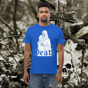 Man wearing a navy Death’s Embrace t-shirt featuring skeleton holding a woman, gothic lettering reading “Death,” standing before a weathered grave.