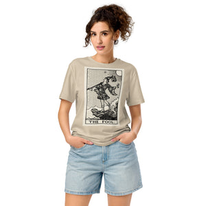 Mid-light organic cotton t-shirt featuring The Fool tarot card with cliff, dog, and sun in high-contrast woodcut rendering.