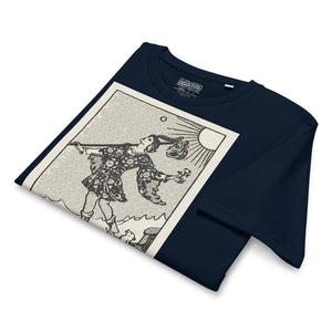 Mid-light organic cotton t-shirt featuring The Fool tarot card with cliff, dog, and sun in high-contrast woodcut rendering.