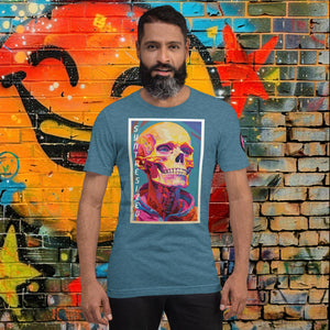 Man wearing a heather deep teal Synthesized Futility Core Tee with bright multicolor skull artwork and “SYNTHESIZED” text, standing before graffiti mural.