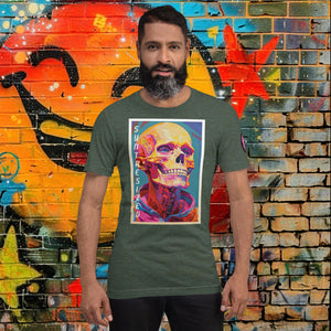 Man wearing a heather forest Synthesized Futility Core Tee with bright multicolor skull artwork and “SYNTHESIZED” text, standing before graffiti mural.