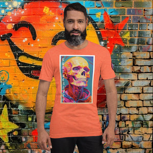 Man wearing a heather orange Synthesized Futility Core Tee with bright multicolor skull artwork and “SYNTHESIZED” text, standing before graffiti mural.