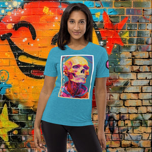 A woman wearing an aqua triblend Synthesized Futility Premium Tee with vibrant stylized skull, graffiti background with orange and blue tones.