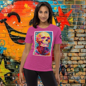 A woman wearing a berry triblend Synthesized Futility Premium Tee with vibrant stylized skull, graffiti background with orange and blue tones.