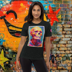 A woman wearing a charcoal black triblend Synthesized Futility Premium Tee with vibrant stylized skull, graffiti background with orange and blue tones.