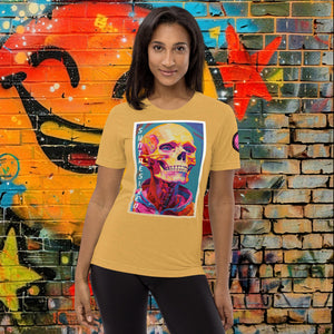 A woman wearing a mustard triblend Synthesized Futility Premium Tee with vibrant stylized skull, graffiti background with orange and blue tones.