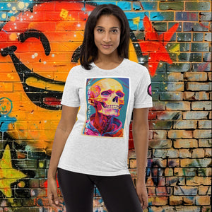 A woman wearing a white fleck triblend Synthesized Futility Premium Tee with vibrant stylized skull, graffiti background with orange and blue tones.