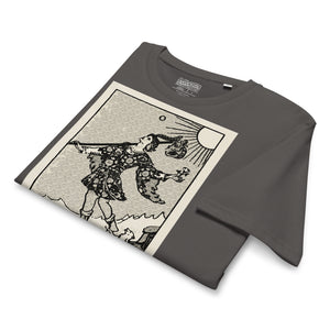 Mid-light organic cotton t-shirt featuring The Fool tarot card with cliff, dog, and sun in high-contrast woodcut rendering.