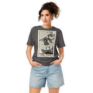 Mid-light organic cotton t-shirt featuring The Fool tarot card with cliff, dog, and sun in high-contrast woodcut rendering.
