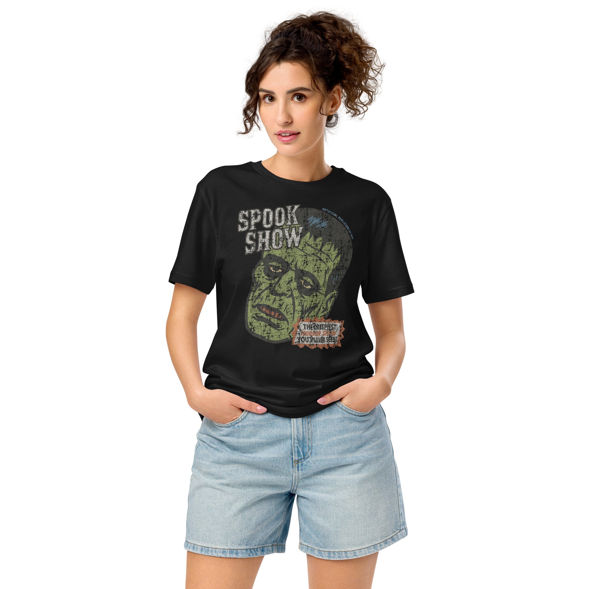 A woman standing wearing a distressed Frankenstein head with “Spook Show” on a premium mid-light organic black tee.