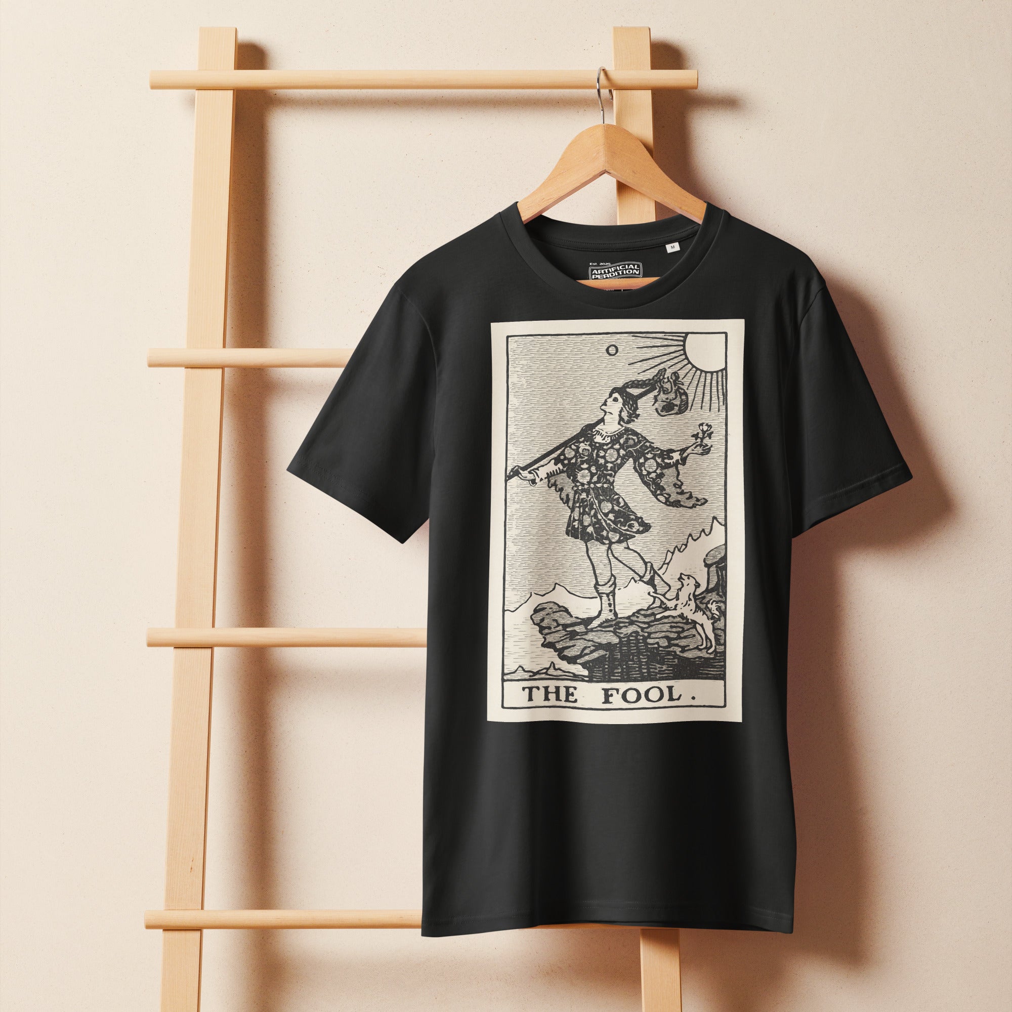 Mid-light organic cotton t-shirt featuring The Fool tarot card with cliff, dog, and sun in high-contrast woodcut rendering.