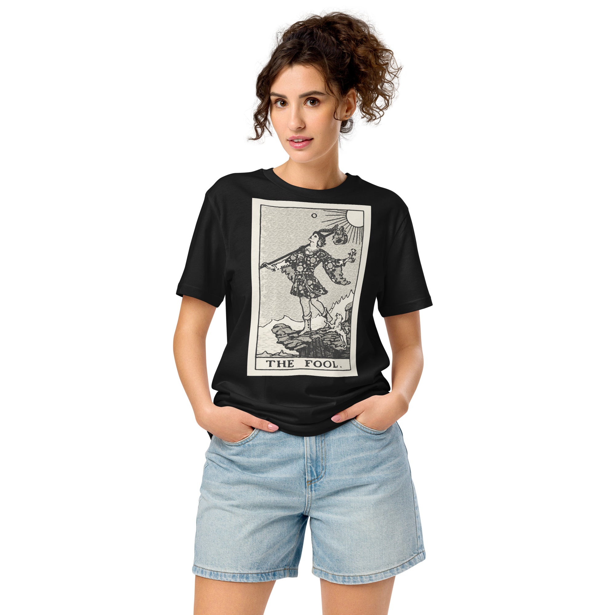 Mid-light organic cotton t-shirt featuring The Fool tarot card with cliff, dog, and sun in high-contrast woodcut rendering.