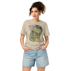 A woman standing wearing a distressed Frankenstein head with “Spook Show” on a premium mid-light organic desert dust tee.